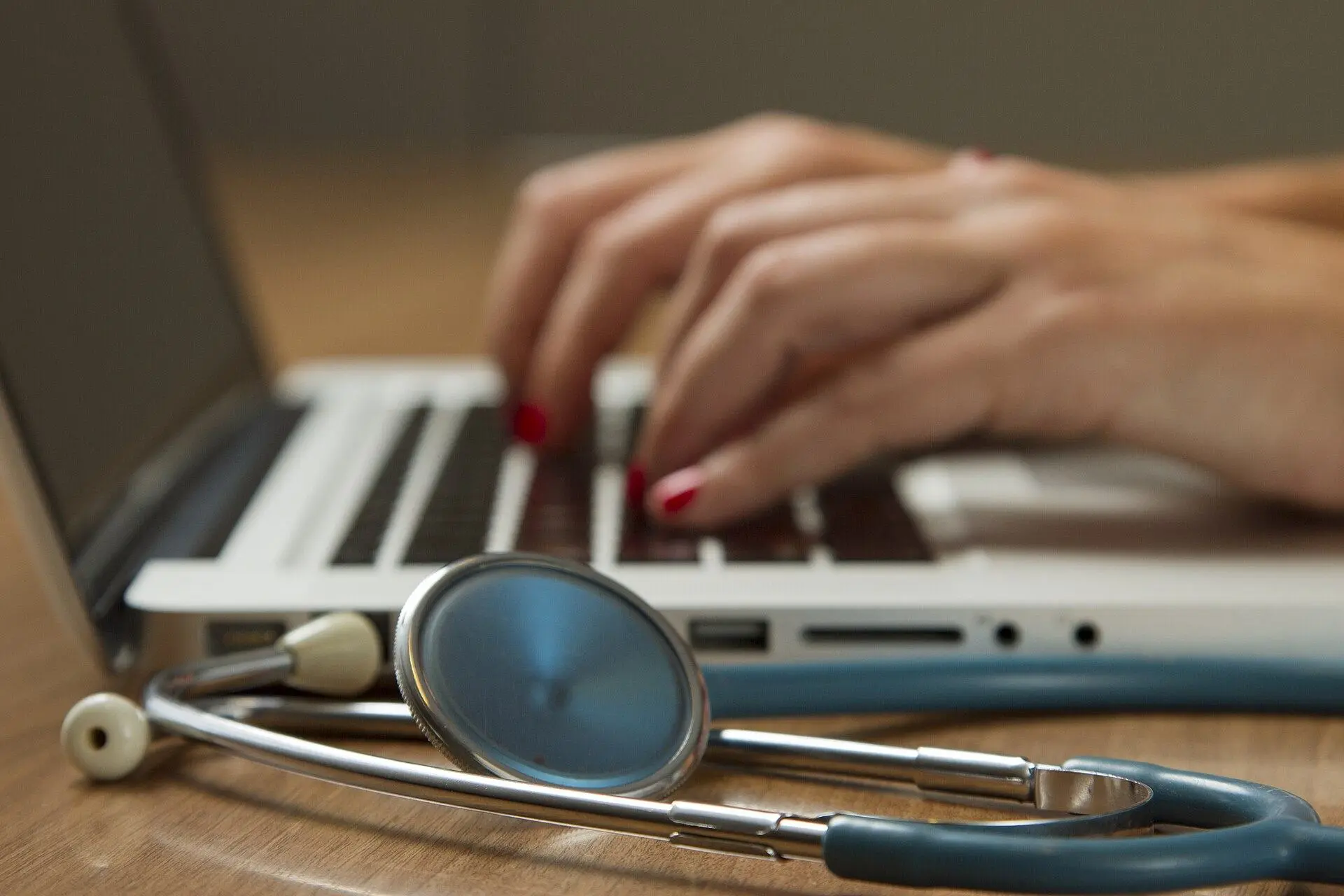 A stethoscope in front of a laptop on which a healthcare professional is typing